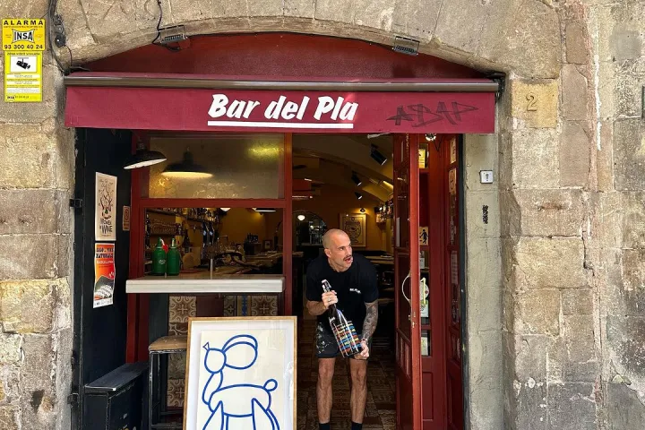 Open door under a stone arch and a red awning displaying the bar's sign.
