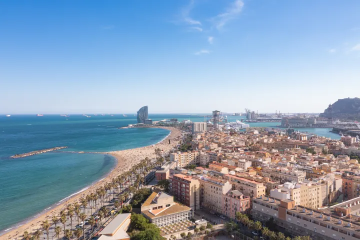 La playa de la Barceloneta y su paseo vistos desde el cielo, el barrio en forma de damero detrás y Port Vell al fondo