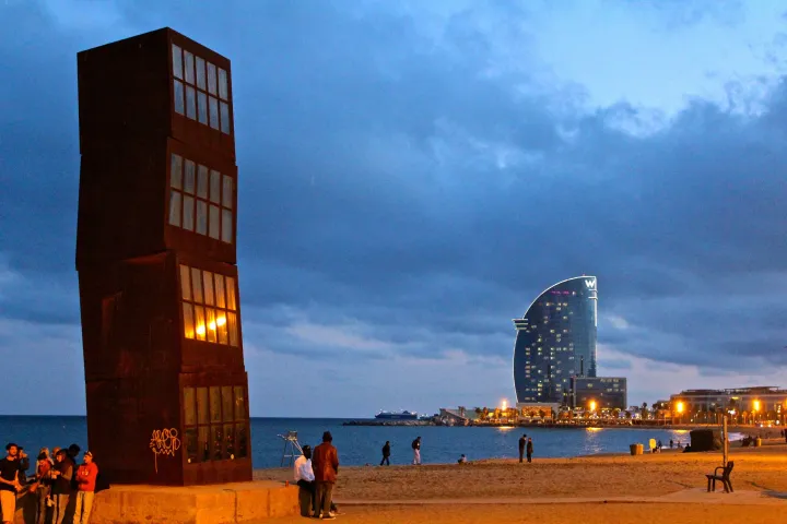A escultura L'Estel Ferit de Rebecca Horn na praia da Barceloneta ao entardecer, com o hotel W ao fundo