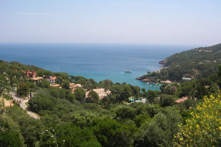 Die Bucht von Sa Riera erscheint zwischen den bewaldeten Hügeln und den Häusern, mit Blick auf das Mittelmeer.