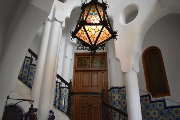 El interior blanco y luminoso de Torre Bellesguard, con su lámpara, la escalera y el zócalo de cerámica