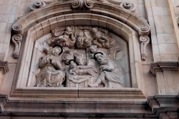 Rilievo scolpito della Natività: Maria, Giuseppe, il Bambino nella mangiatoia e il bue, sovrastati da angeli con l'iscrizione Gloria in excelsis Deo