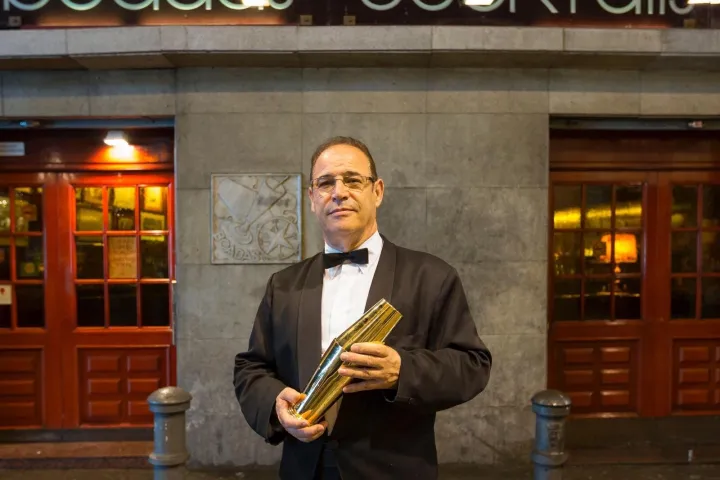 Ein Barkeeper in dunkler Jacke und Fliege vor dem Eingang von Boadas.