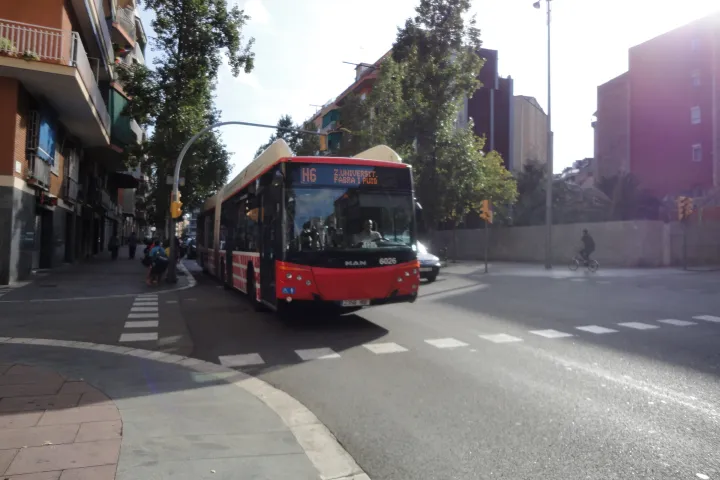 Um ônibus articulado vermelho e branco da linha H6 da TMB em uma avenida de Barcelona