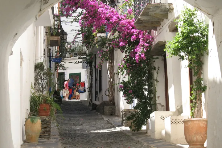 The carrer des Call winds through white houses under an arch, with balconies adorned with bougainvillea.