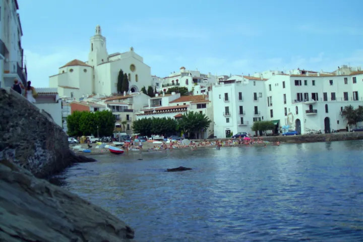 Santa Maria Church towers over the white houses and the Portdoguer beach, as seen from the shoreline.