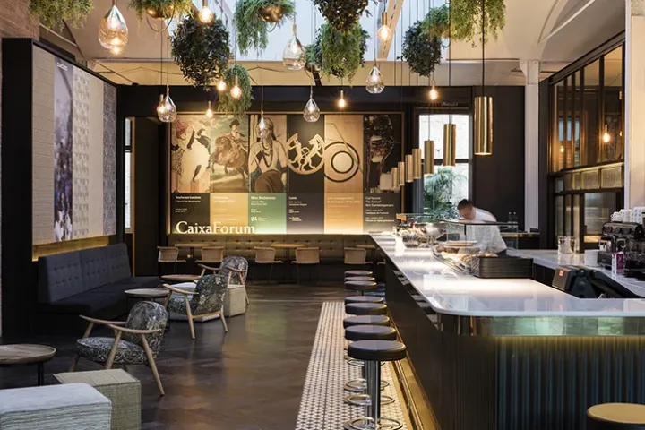 The café at CaixaForum, with its long counter, golden pendant lights, and plants hanging from the ceiling