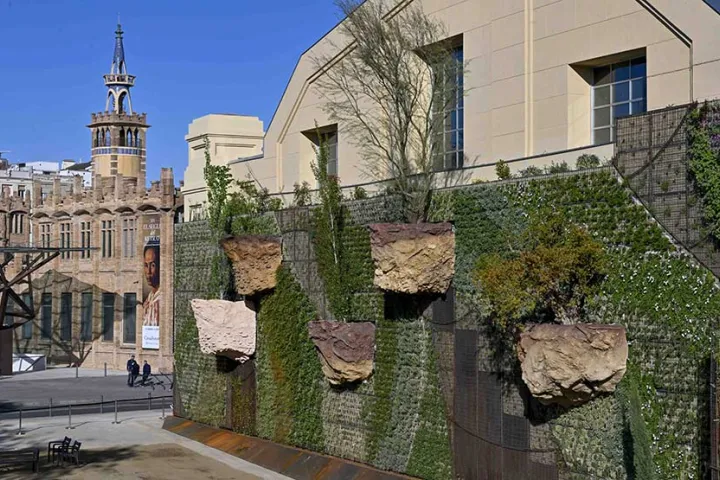 A vertical garden planted on protruding stone blocks, in front of the brick tower of the former Casaramona factory