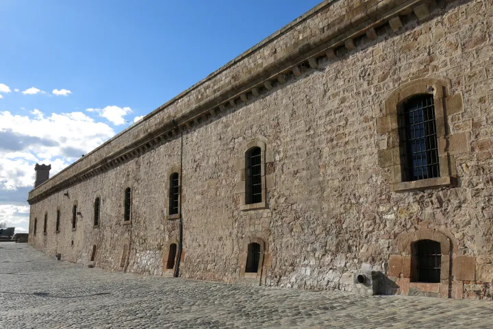El camino empedrado que bordea la muralla de Marina del castillo de Montjuïc, bajo un cielo azul