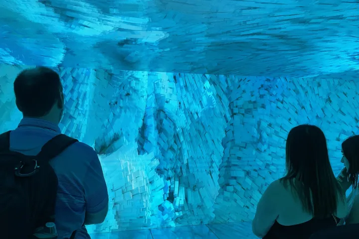 Visitantes en el Cubo de Gaudí de la Casa Batlló, rodeados de una proyección azul animada en las paredes y el techo
