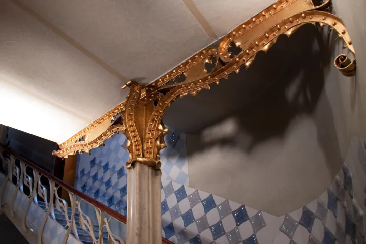 Escalera de honor de la Casa Batlló, barandilla de hierro forjado y columna dorada bajo un techo ondulado