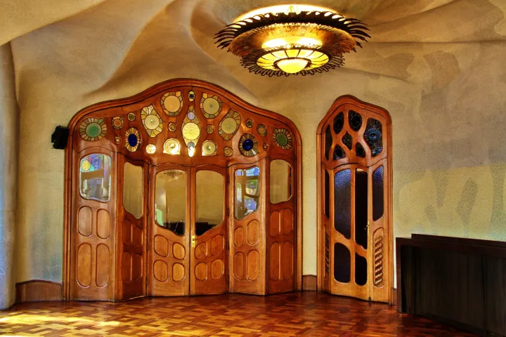 Las puertas de madera tallada con vitrales redondos del piso noble, bajo un techo ondulado y un candelabro en forma de sol