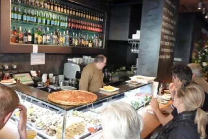 Customers at the counter in front of the tapas and bottles at Cervecería Catalana.