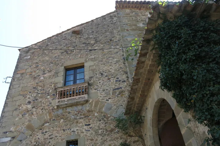 La façade en pierre du château de Púbol présente une fenêtre à balcon sculpté, à côté d’un porche bordé de lierre.