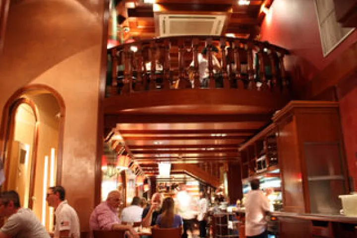 Lively dining room and counter at Ciudad Condal under a wooden balcony.