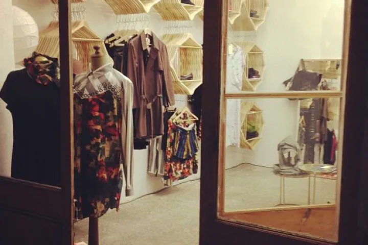 Entrada abierta de Colmado, ropa colgada y expositores de madera en el interior.