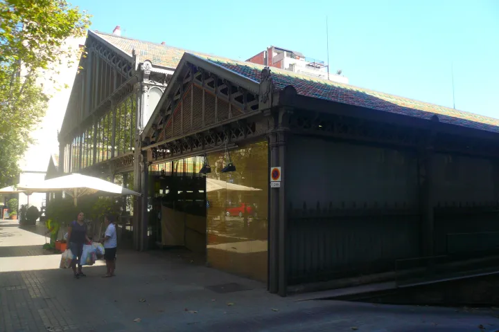 Die Fassade aus Gusseisen und Glas des Mercat de la Concepció von der Straße aus gesehen, unter den Bäumen