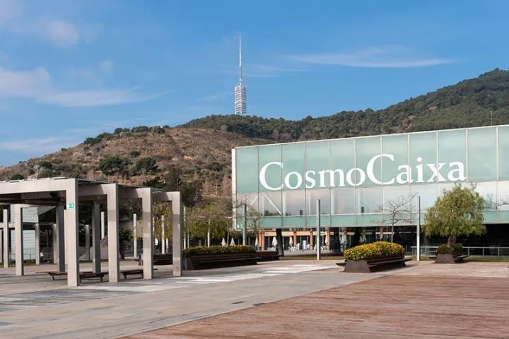 La façade vitrée du CosmoCaixa portant son nom en grandes lettres, au pied de la colline du Tibidabo et de sa tour de télécommunications