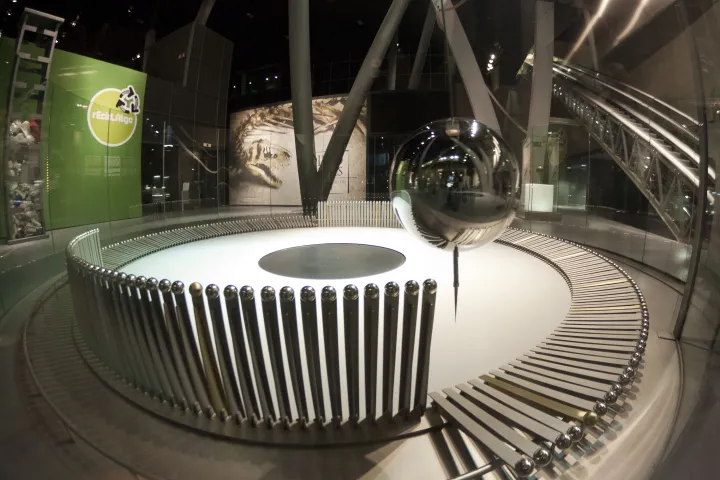 La sphère métallique du pendule de Foucault suspendue au-dessus de son cercle de quilles, dans le hall du musée