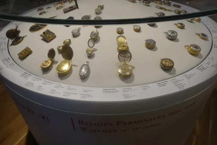 Uma vitrine circular apresentando dezenas de antigos relógios de bolso, em ouro e prata
