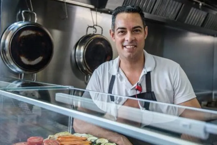 The chef of El Peixet dels Encants behind his counter, tomatoes, grilled vegetables, and croquettes on display