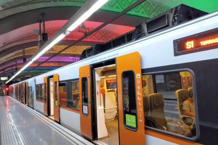 Train FGC blanc et orange de la ligne S1 portes ouvertes, quai de Plaça de Catalunya sous une voûte éclairée
