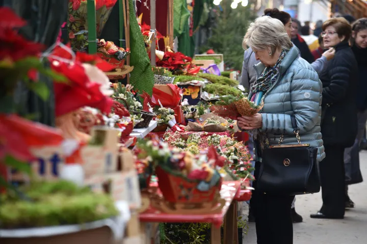 Eine Besucherin wählt einen Blumenstrauß vor einem Stand der Fira de Nadal aus, der mit Pflanzen, Kränzen und Weihnachtsgeschenken beladen ist