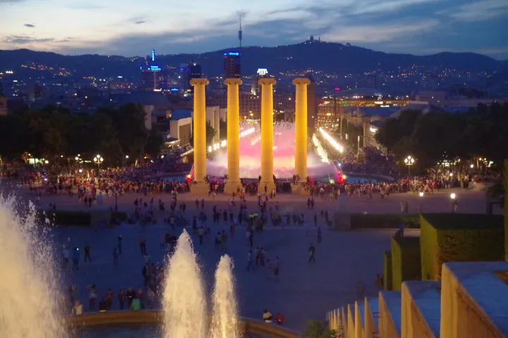 View from the terraces of the Palau Nacional at dusk: the illuminated fountain, the four columns, and the city