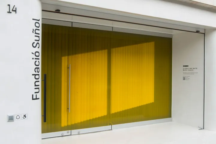 Die weiße Fassade der Fundació Suñol, deren Schaufenster mit gelbem, transluzentem Glas verkleidet ist
