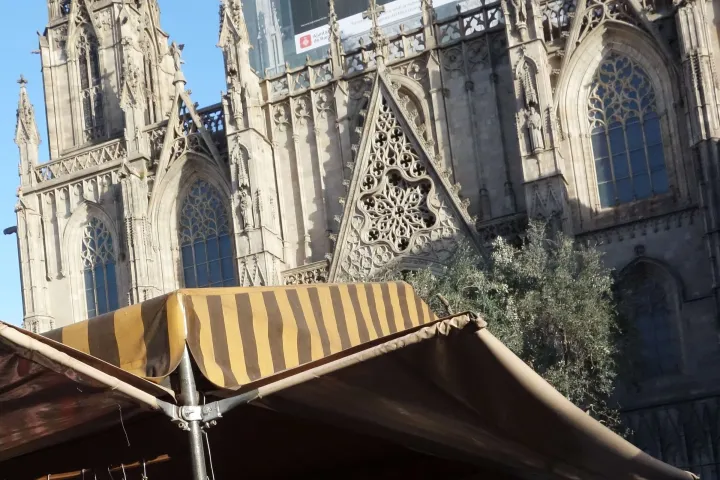 The Gothic facade of Barcelona Cathedral towering over the striped canopies of the Gothic Market stalls