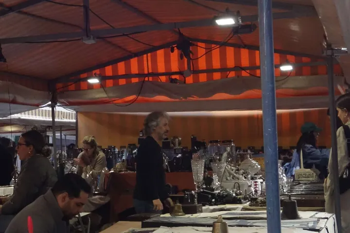 Un antiquaire derrière son étal d'argenterie, de verrerie et d'objets anciens au Mercat Gòtic