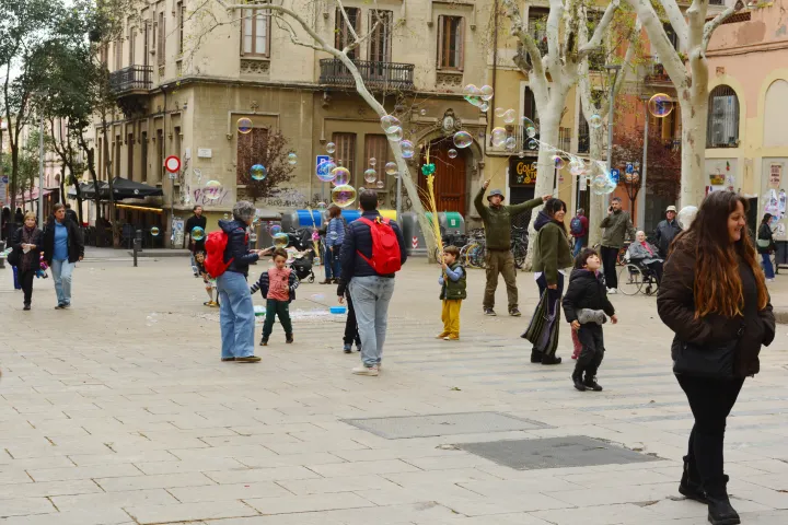 Dei bambini giocano con le bolle di sapone sulla Plaça de la Virreina, tra i platani e le facciate di Gràcia