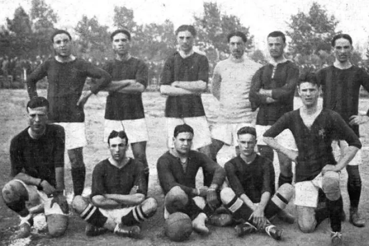 Die Spieler des FC Barcelona posieren in zwei Reihen auf einem Spielfeld im Parc de la Ciutadella im Jahr 1910, auf einer schwarz-weißen Fotografie.