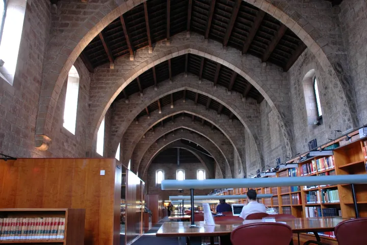 Un'antica sala ospedaliera con grandi archi in pietra e soffitto in legno, trasformata in sala di lettura della Biblioteca de Catalunya