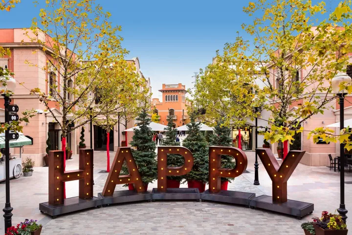 Avenida de La Roca Village con sus tiendas, árboles y letras luminosas HAPPY.