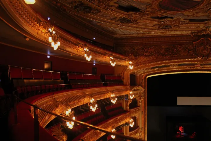 Les niveaux de loges dorées du Liceu vus depuis un balcon latéral, leurs appliques allumées et le cadre de scène à droite