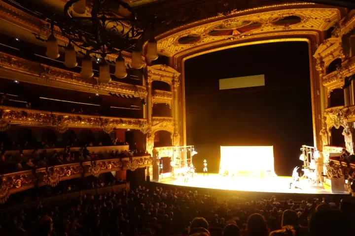 La scène éclairée du Liceu pendant une représentation, vue depuis le fond de la salle comble