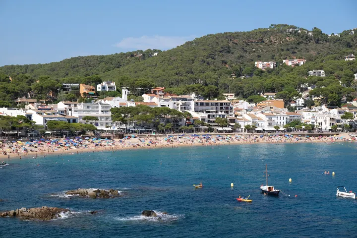 Der Strand von Llafranc erstreckt sich vor den Häusern und bewaldeten Hügeln, mit Booten, die vor Anker liegen.