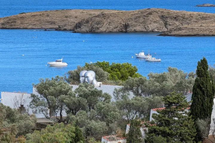 Die weißen Mauern und Olivenbäume des Gartens überblicken die Bucht von Portlligat, wo mehrere Boote vor Anker liegen.