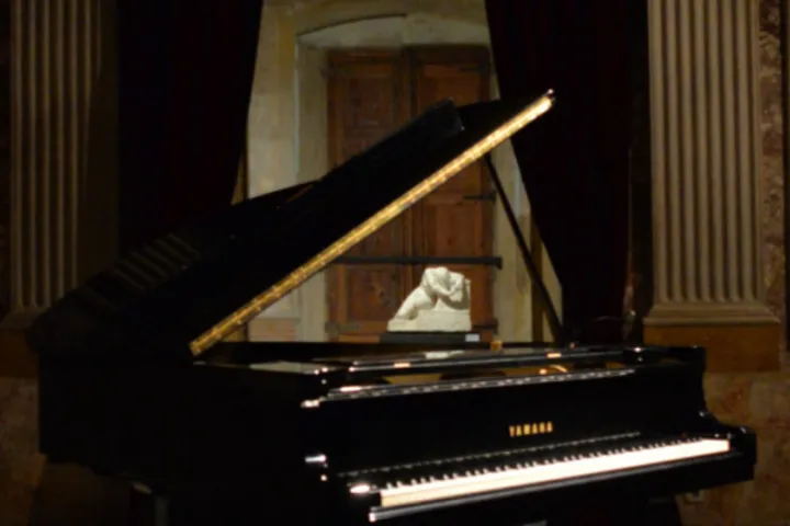 An open grand piano in a dimly lit room with stucco-adorned walls, in front of a marble sculpture