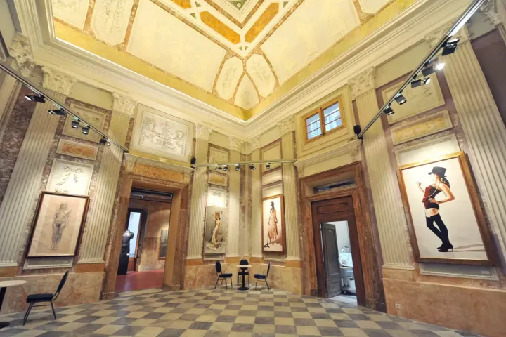 A room with gilded moldings and a painted ceiling, marble checkerboard floor, where large contemporary portraits are displayed