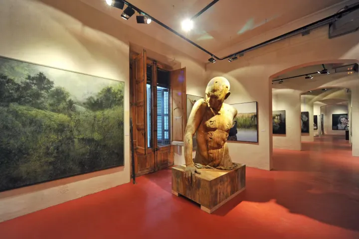 A wooden sculpture of a man's torso in the center of a room with a red floor, surrounded by large figurative paintings