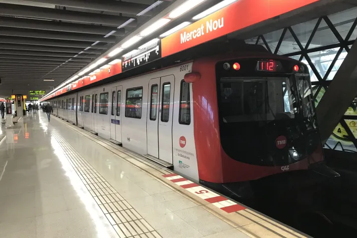 Trem de metrô TMB série 6000 vermelho e branco na plataforma sob a faixa vermelha da estação Mercat Nou (L1)