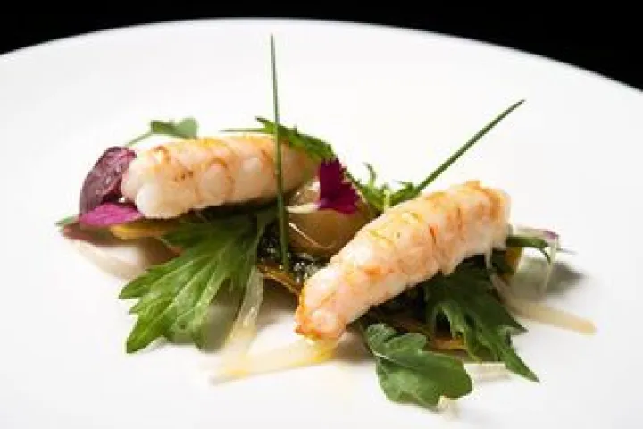 Two langoustines arranged with green leaves on a white plate.
