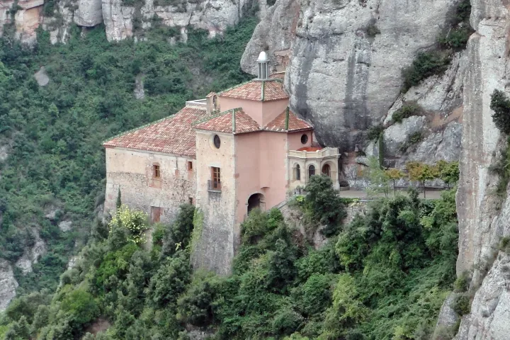 A capela da Santa Cova está encostada ao penhasco, acima de uma encosta arborizada de Montserrat.