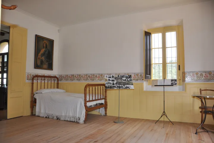 A recreated room with yellow walls, featuring a wooden bed, a painted frieze, and a window open to the countryside