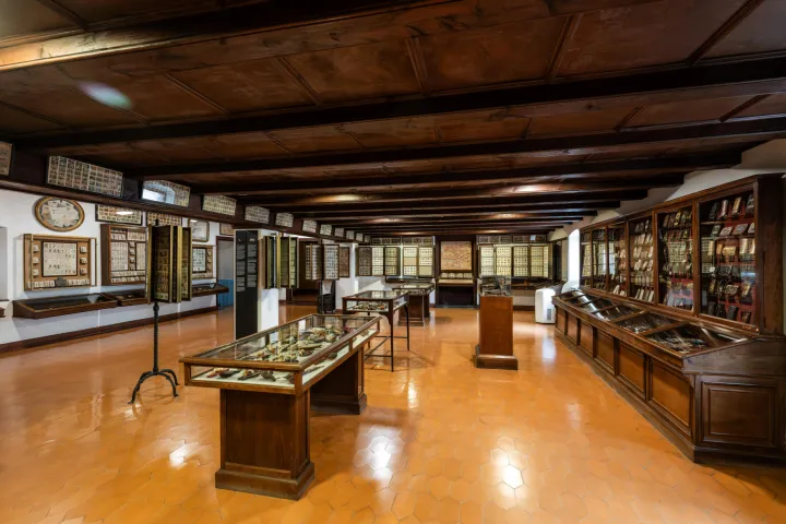 Uma sala com teto de madeira e piso de ladrilhos, revestida de vitrines e quadros cheios de pequenos objetos de coleção