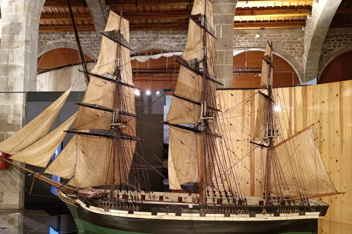 Una gran maqueta de velero con todas las velas desplegadas, bajo los arcos de piedra de las Drassanes