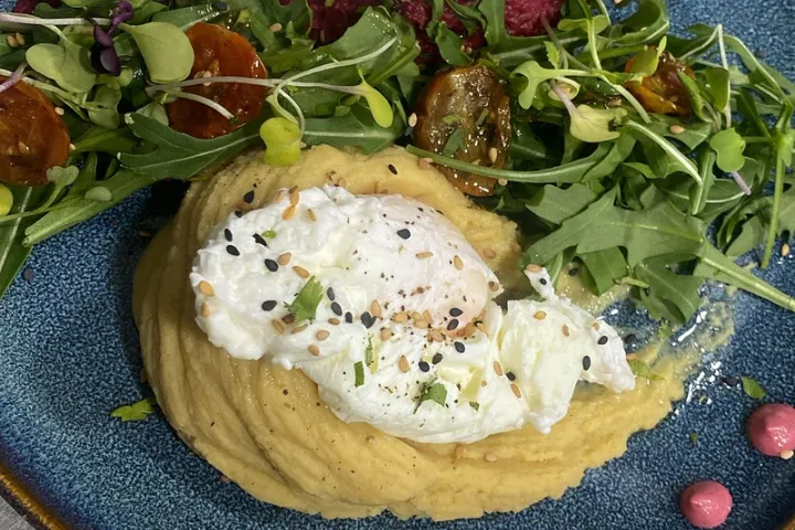 Two poached eggs with colorful preparations and a salad on a blue plate.