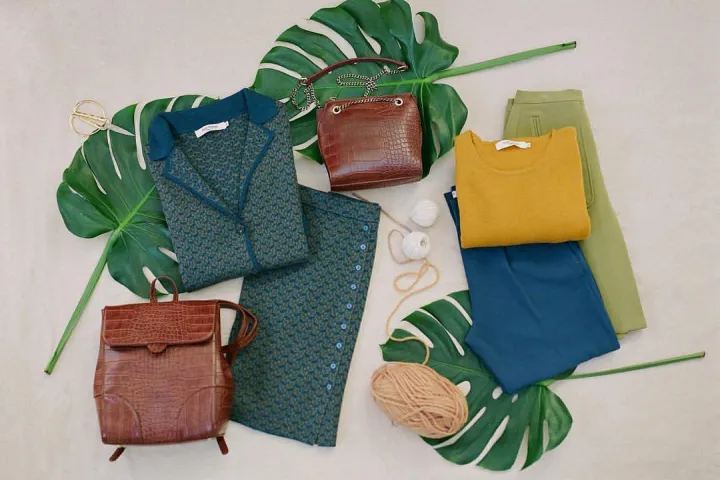 Ropa colorida y bolsos Nice Things dispuestos sobre grandes hojas.